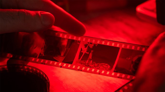 hands holding a strip of celluloid film in a dark room with red light