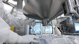 White pills fall from a silver funnel at a manufacturing facility.