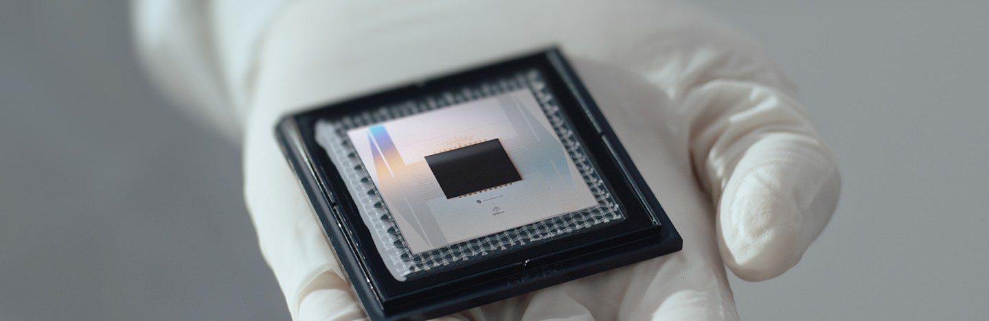 A gloved hand holds a shiny metallic quantum computing chip.