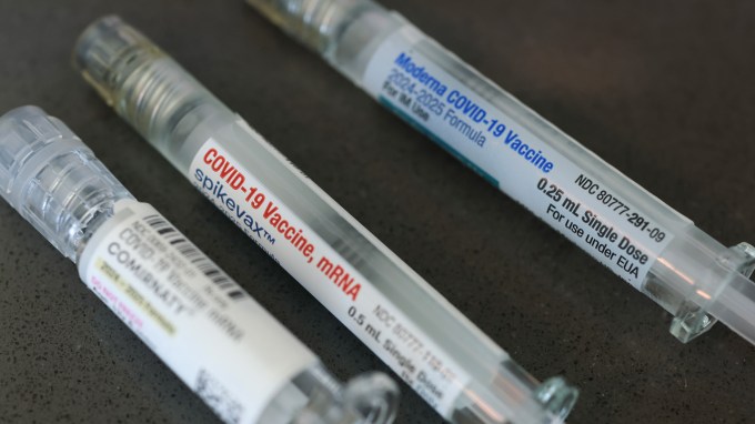 Three labeled COVID-19 vaccine syringes lie on a dark surface.