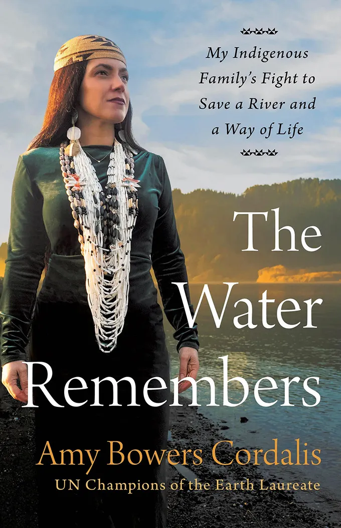 The cover of "The Water Remembers," showing a woman standing against a backdrop of water and land.