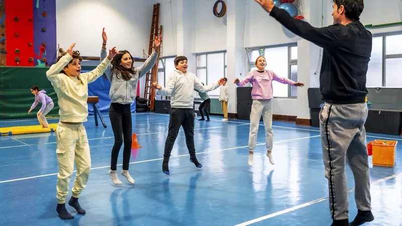 a group of middle school kids doing jumping jacks in a gym as directed by their teacher