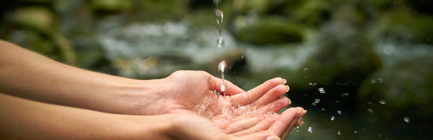 A stream of water breaks up into droplets as it falls into a person's hands.