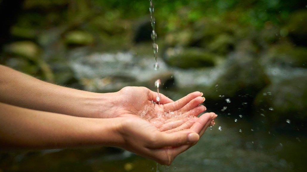 A stream of water breaks up into droplets as it falls into a person's hands.