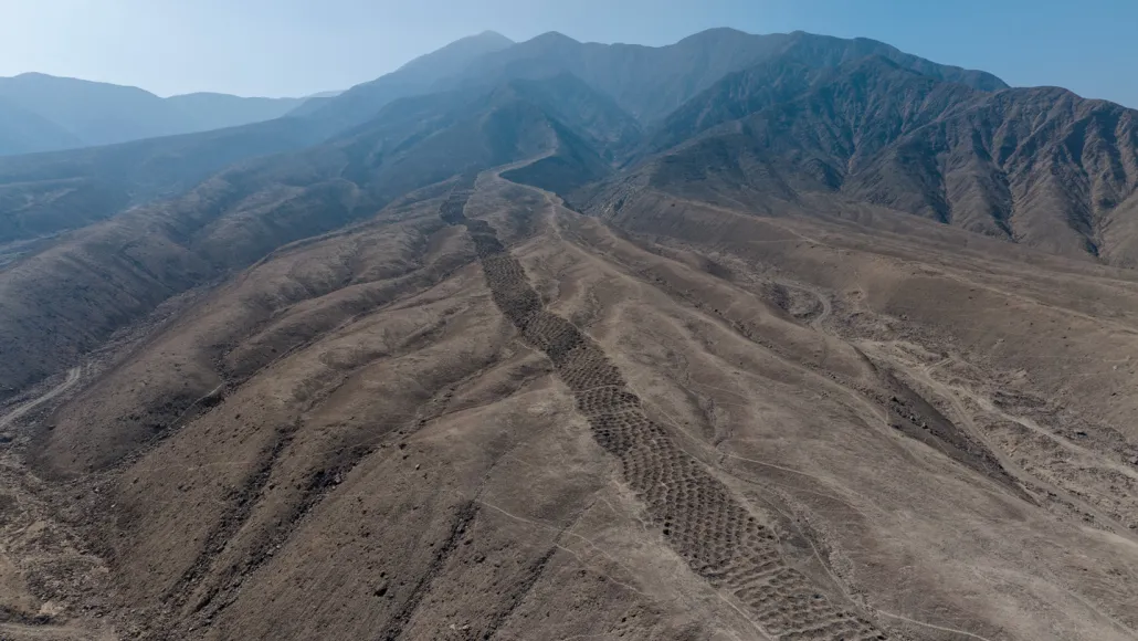 This aerial view of the brown foothills of the Andes shows a ridgetop series of earthen holes, part of an ancient mysterious monument that stretches 1.5 kilometers.