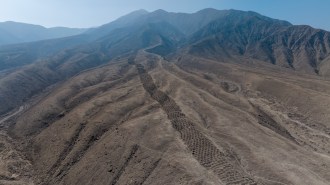 This aerial view of the brown foothills of the Andes shows a ridgetop series of earthen holes, part of an ancient mysterious monument that stretches 1.5 kilometers.