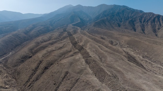 This aerial view of the brown foothills of the Andes shows a ridgetop series of earthen holes, part of an ancient mysterious monument that stretches 1.5 kilometers.