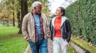Two older people walk on a foliage-lined path.