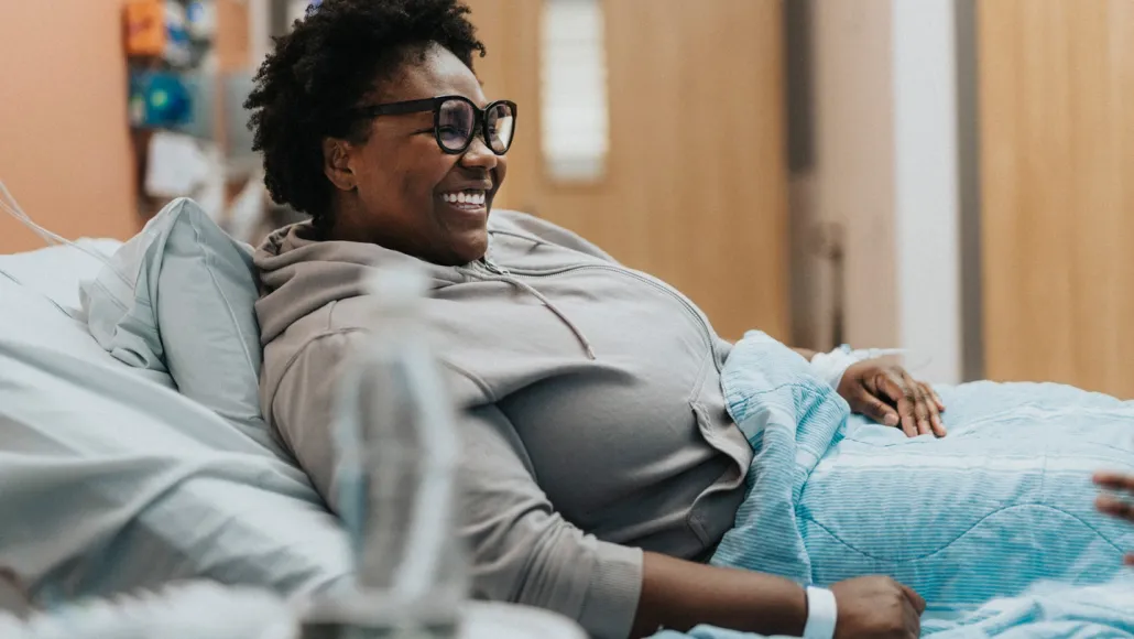 A patient smiles while resting in a hospital bed.