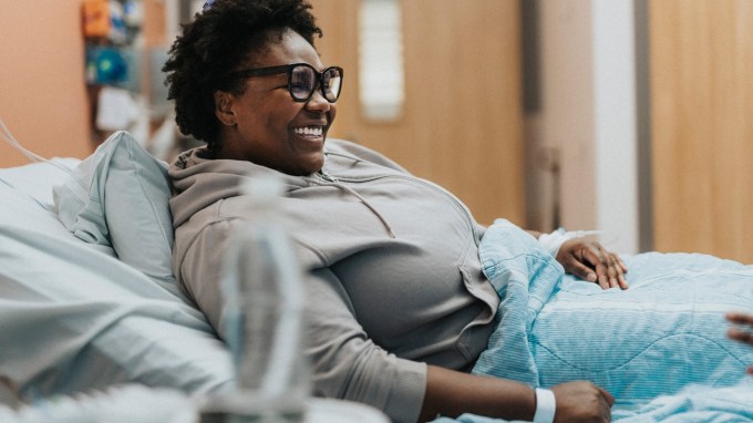 A patient smiles while resting in a hospital bed.