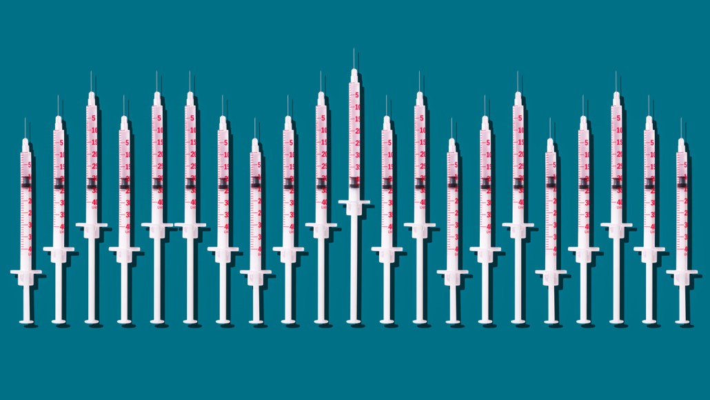 A row of 21 hypodermic needles of varying lengths are lined up, needles pointing up, against a blue background.