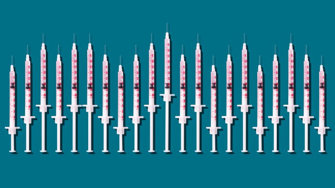A row of 21 hypodermic needles of varying lengths are lined up, needles pointing up, against a blue background.
