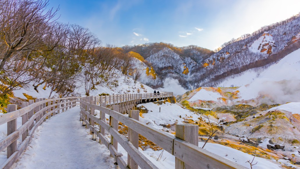A snow covered bridge winds between tree-lined mountains.