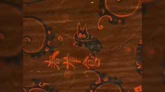 A closeup of a bowl found in an ancient tomb includes a depiction of a cat with tall fluffy ears, claws visible, some spots in its black back and a striped tail, reminiscient of a leapard cat.
