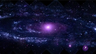 A large spiral galaxy glows in purple light.