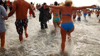 people in bathing suits on the shore in Coney Island, NY running into the water.