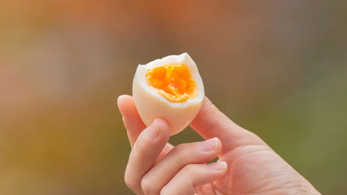 A hand holding a hard-boiled egg with a bite taken out of it, exposing the yolk