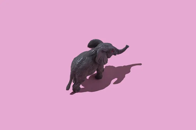 A toy elephant looks like it's walking across a pink background in this image shot from overhead.