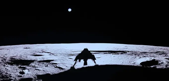The shadow of a moon lander is seen on the surface of the moon while a round circle, Earth, hangs in the dark beyond the moon.