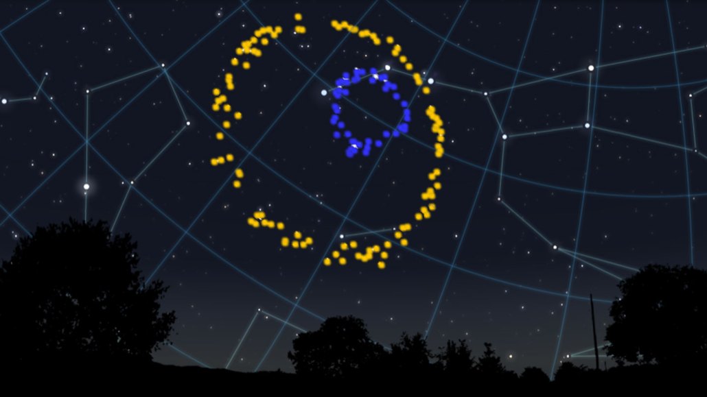 A big yellow ring encircles a smaller blue ring against a backdrop of stars and constellations