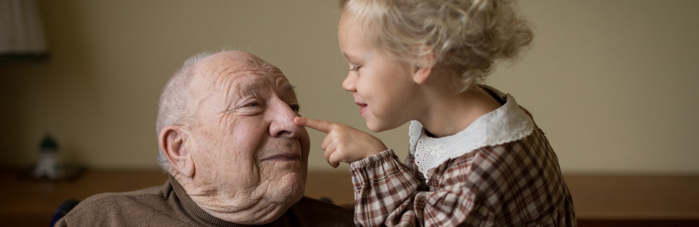 A young child pokes an elderly man on the nose