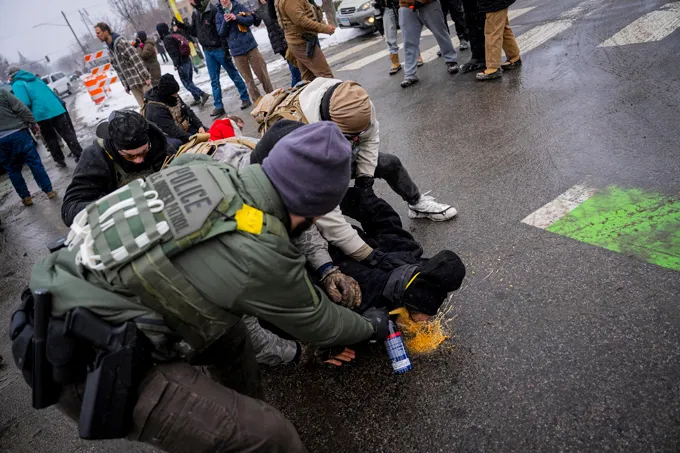 A man is held down by multiple people while pepper spray is sprayed into his face.