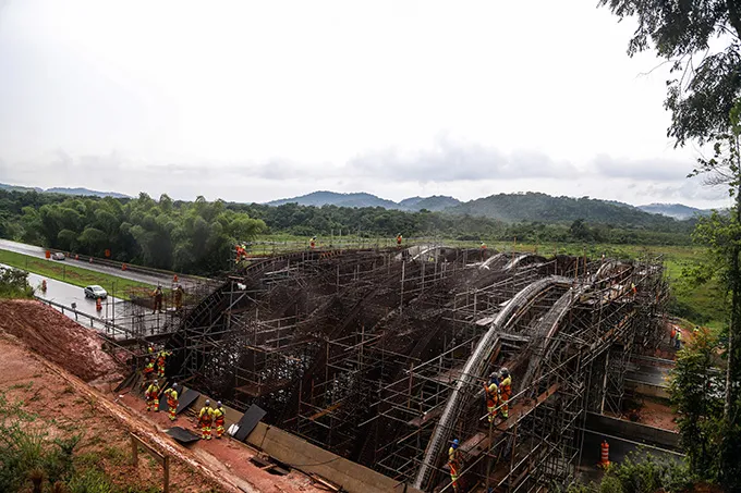 A photo of what looks like a bridge construction over a highway with several builders working on it
