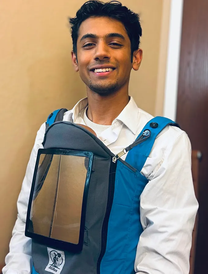 A young man in a button-up shirt wears a baby carrier with a massive transparent panel on his front