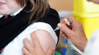 A close-up of a young girl's shoulder getting an injection from an older woman