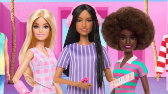Three barbie dolls stand in front of a pink background.