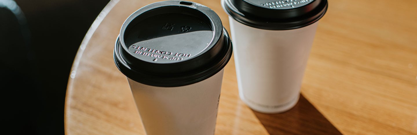 Two cups of takeout coffee or tea sit on a table.