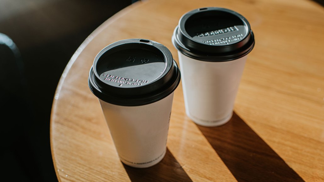 Two cups of takeout coffee or tea sit on a table.