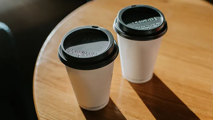 Two cups of takeout coffee or tea sit on a table.