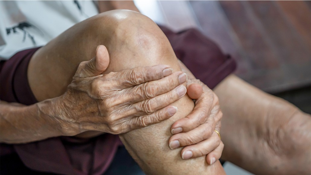 An older person clutches their knee.