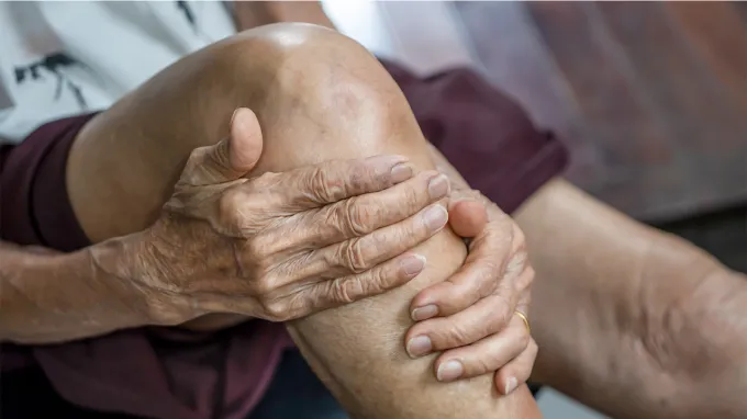 An older person clutches their knee.
