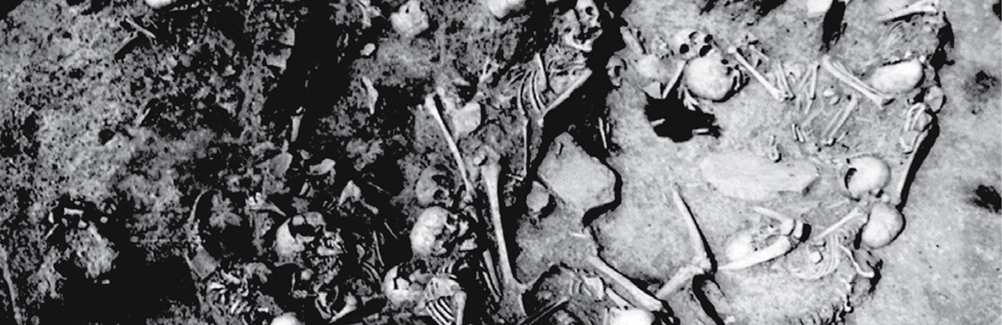 A black and white photo shows human skulls and other bones in a circular pit.