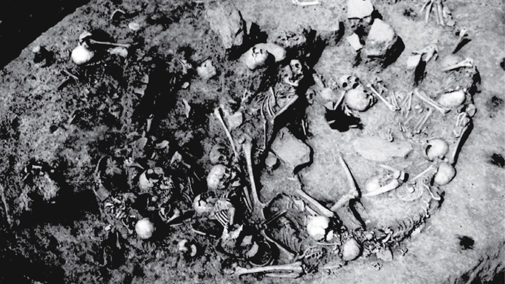 A black and white photo shows human skulls and other bones in a circular pit.