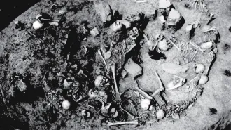 A black and white photo shows human skulls and other bones in a circular pit.
