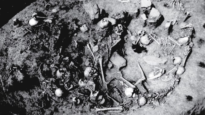 A black and white photo shows human skulls and other bones in a circular pit.