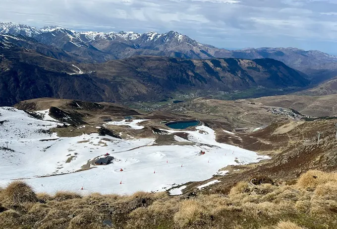 A ski resort in the French mountains. A track of artificial snow is surrounded by green grass.