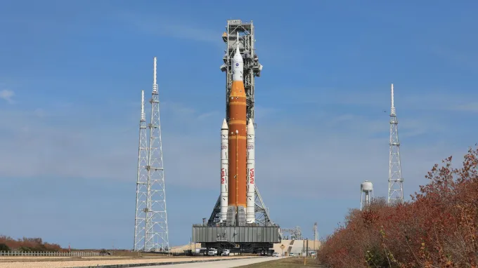 An orange rocket stands out against a blue sky.