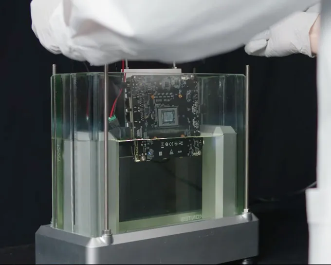 A black computer motherboard being dipped into an oil-like liquid.