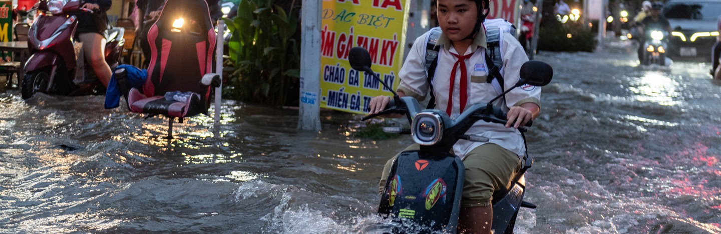 A person drives a motorbike through a flooded street.