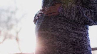 A pregnant woman wearing a sweater places her hands on her belly.