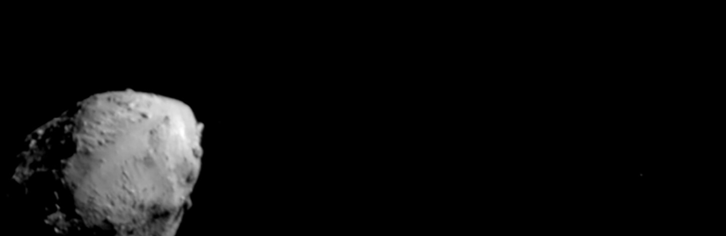 A large grey space rock looms bottom left on a black background. A smaller one hovers at the top and center of the image.