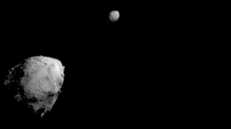 A large grey space rock looms bottom left on a black background. A smaller one hovers at the top and center of the image.