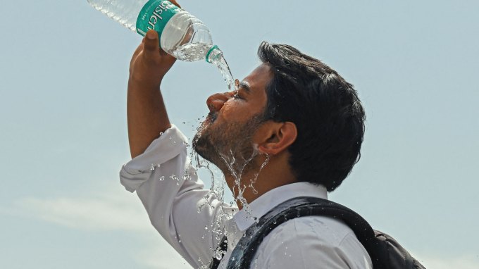 A man pours water from a plastic bottle onto his face.