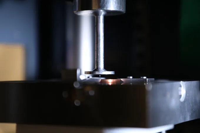A small ball hovers in the narrow opening of a machine that looks like a small press