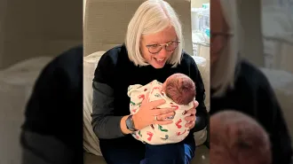 A woman holds a swaddled baby in her lap and looks like she is talking to the infant.