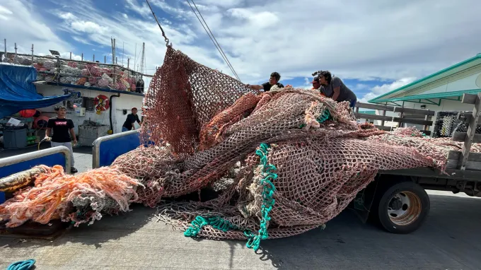 Old, plastic fishing nets being collected into a pile on a trailer.